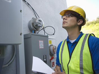 Technician wearing safety hat and vest working looking at a building