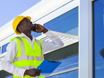 Building engineer wearing a safety vest and hat looking up at a building